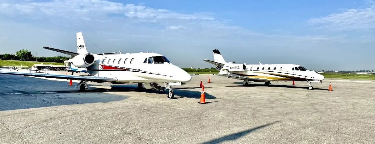 Two business jets on an airport ramp beneath a blue sky.