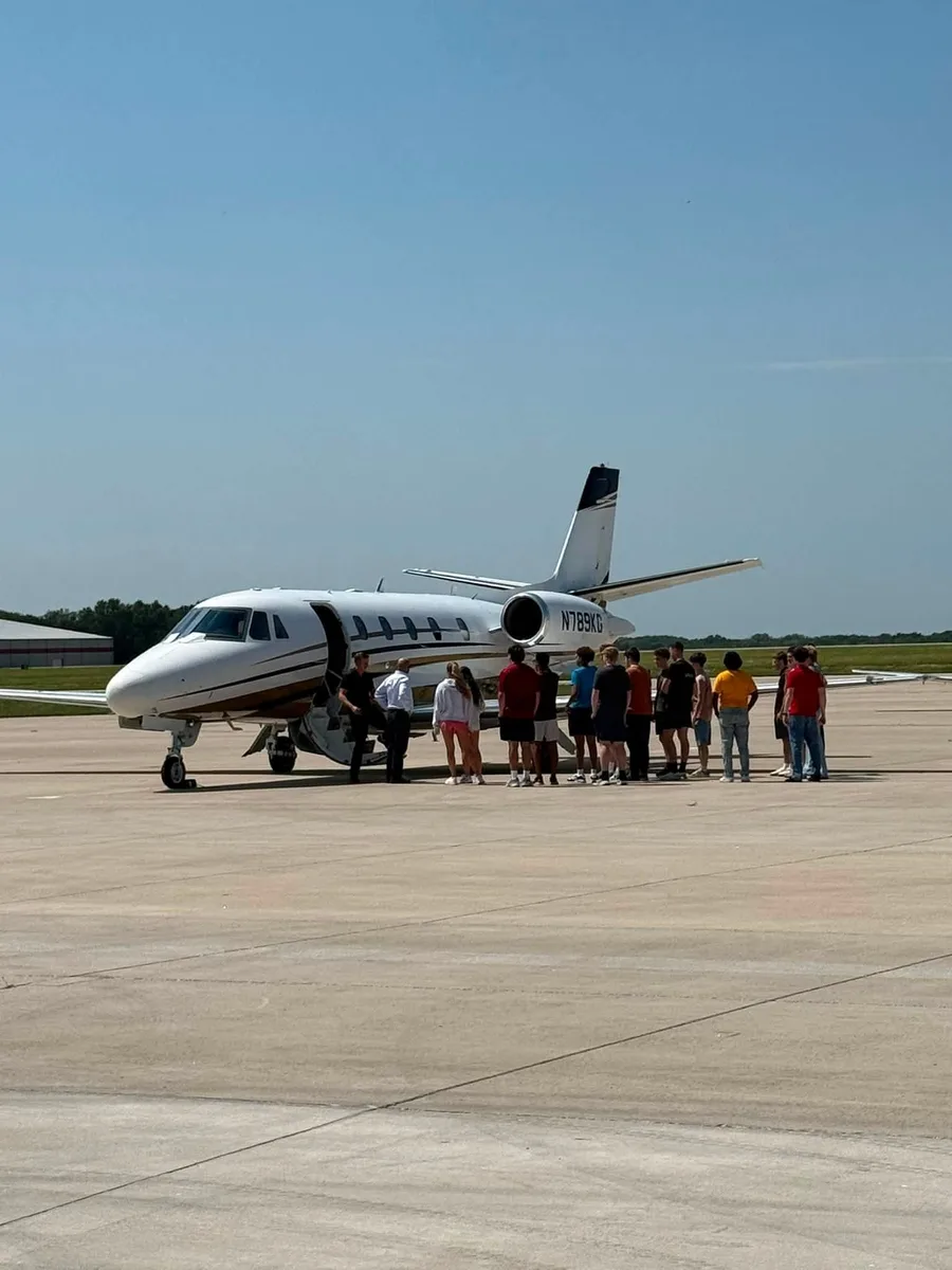 A business jet with a group gathered beside it on an airport ramp.