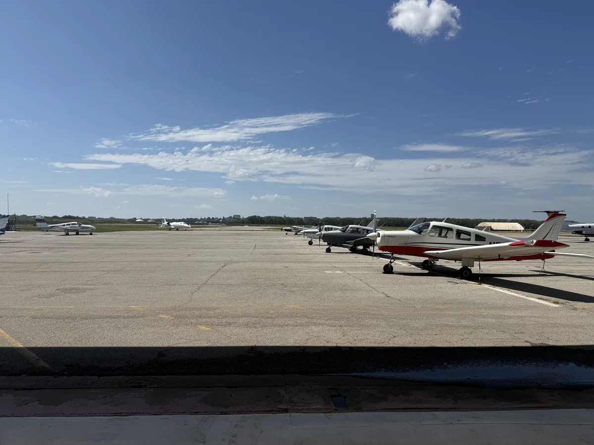 Several small aircraft parked on an airport ramp beneath a blue sky.